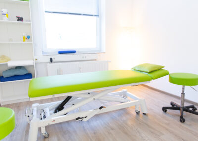 Ein Behandlungszimmer in der Physiotherapie Thomsen und Clauss in Norderstedt mit einer grünen Behandlungsliege, einem passenden Stuhl und einem weißen Regal